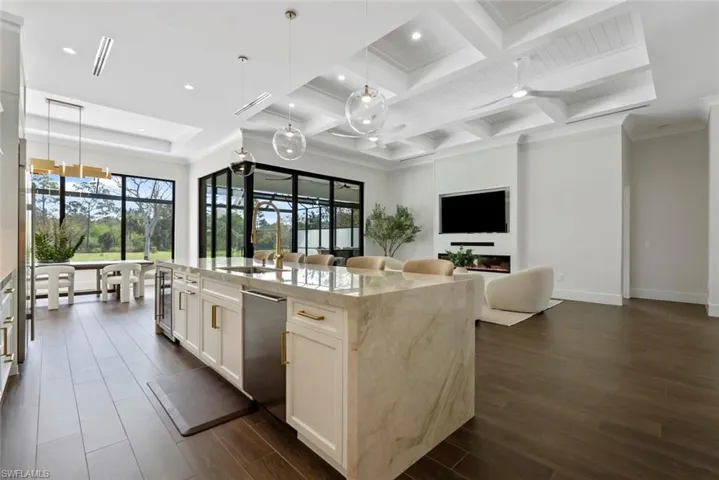 Kitchen with hanging light fixtures, dark wood-type flooring, light stone countertops, and an island with sink
