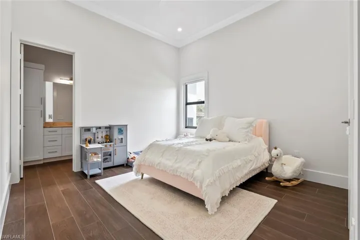 Bedroom featuring connected bathroom, dark wood-type flooring, and ornamental molding