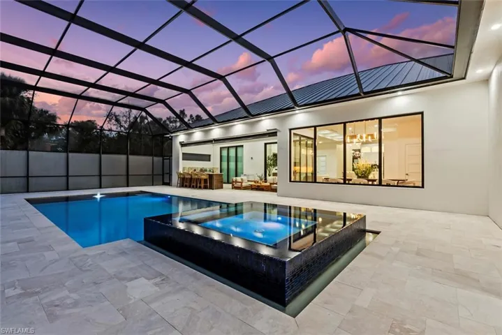 Pool at dusk with an in ground hot tub, a lanai, and a patio area