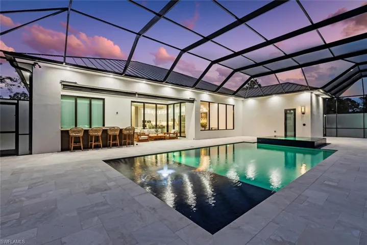 Pool at dusk with a lanai, a patio area, outdoor lounge area, and exterior bar