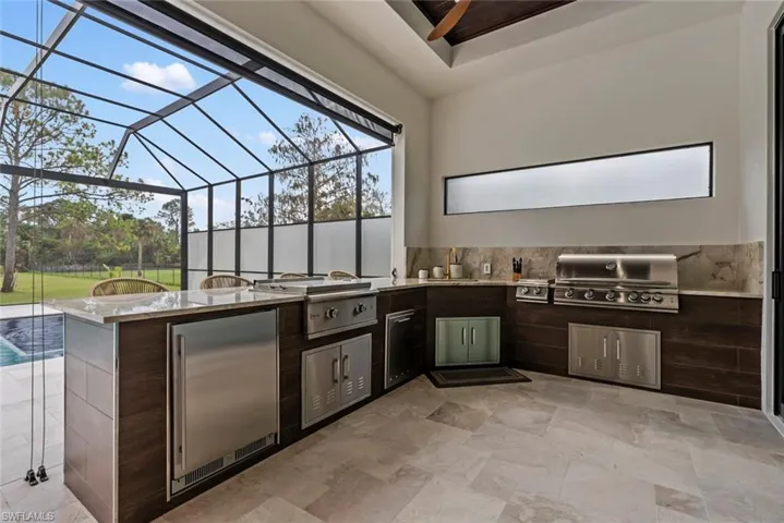 View of patio with exterior kitchen, a grill, and glass enclosure