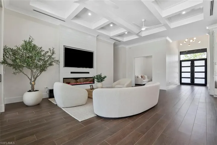 Living room with coffered ceiling, beam ceiling, dark hardwood / wood-style floors, a fireplace, and ceiling fan with notable chandelier