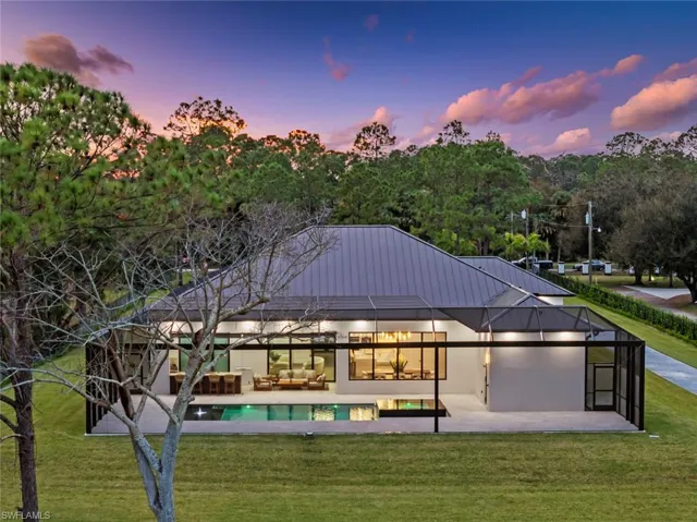 Back house at dusk with an outdoor living space, a patio area, a lawn, and glass enclosure