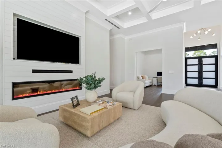 Living room with coffered ceiling, crown molding, wood-type flooring, a large fireplace, and beamed ceiling