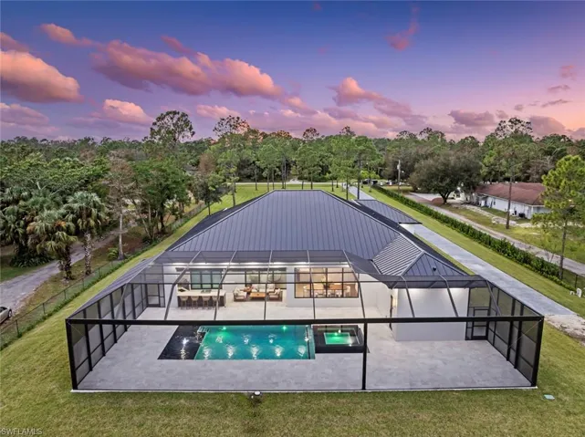 Pool at dusk with a lanai, a patio area, and a lawn