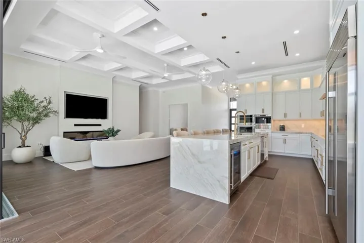 Kitchen featuring sink, white cabinetry, light stone counters, hanging light fixtures, and a kitchen island with sink