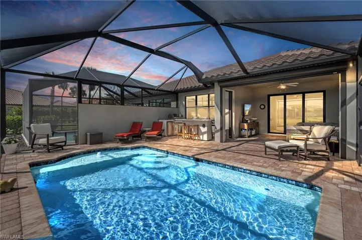 Pool at dusk featuring a patio, exterior bar, outdoor lounge area, ceiling fan, and glass enclosure