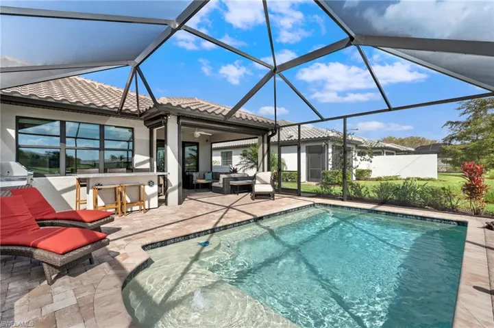 View of pool featuring ceiling fan, a patio, glass enclosure, a bar, and an outdoor hangout area