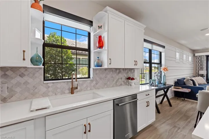 Kitchen with stainless steel dishwasher, a healthy amount of sunlight, sink, and white cabinets