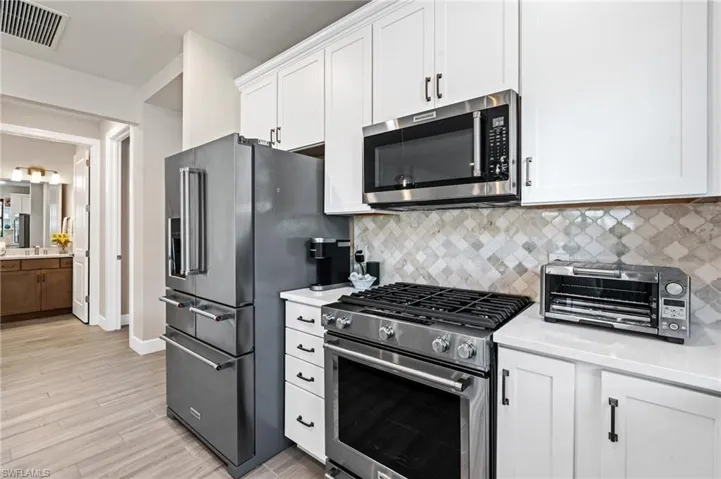 Kitchen with stainless steel appliances, white cabinetry, light wood-type flooring, and decorative backsplash
