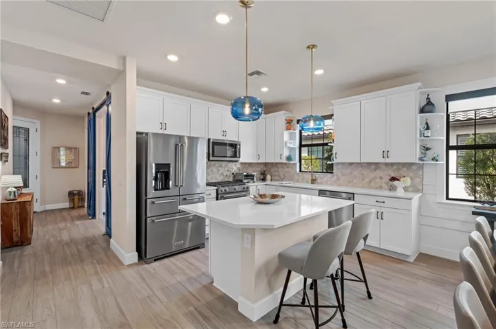 Kitchen featuring a kitchen island, high quality appliances, white cabinets, hanging light fixtures, and a barn door