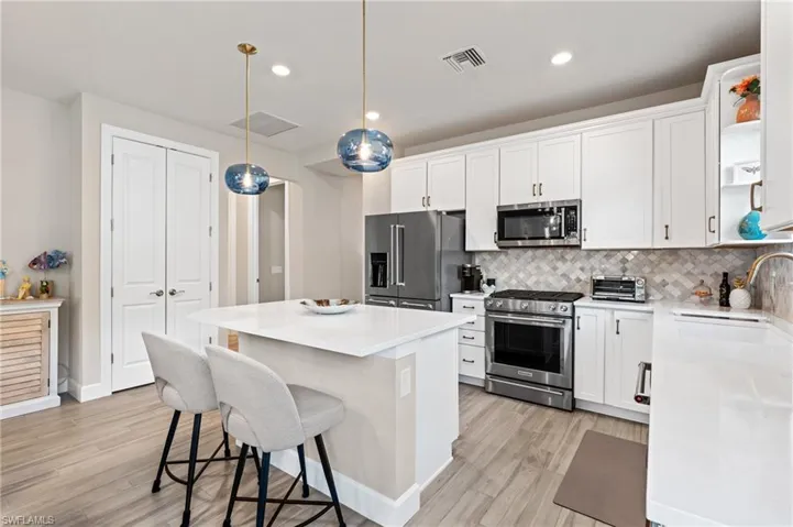 Kitchen with a kitchen island, decorative light fixtures, tasteful backsplash, white cabinetry, and premium appliances