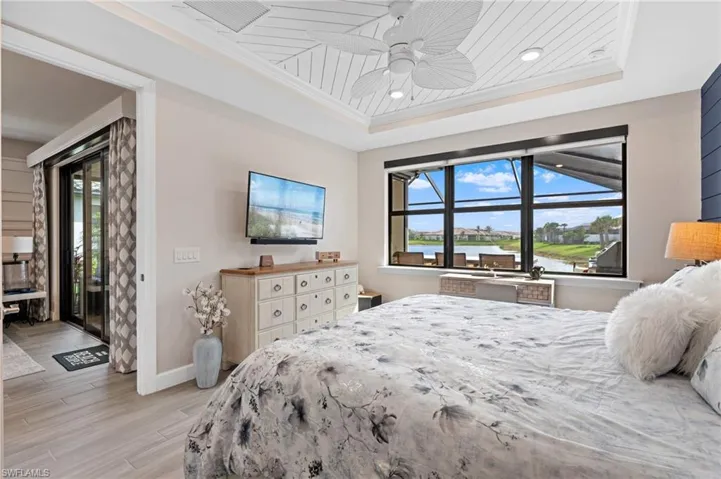 Bedroom featuring ceiling fan, access to exterior, a tray ceiling, ornamental molding, and light hardwood / wood-style floors