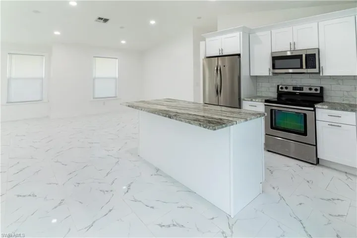 Kitchen with stainless steel appliances, white cabinets, a kitchen island, tasteful backsplash, and recessed lighting