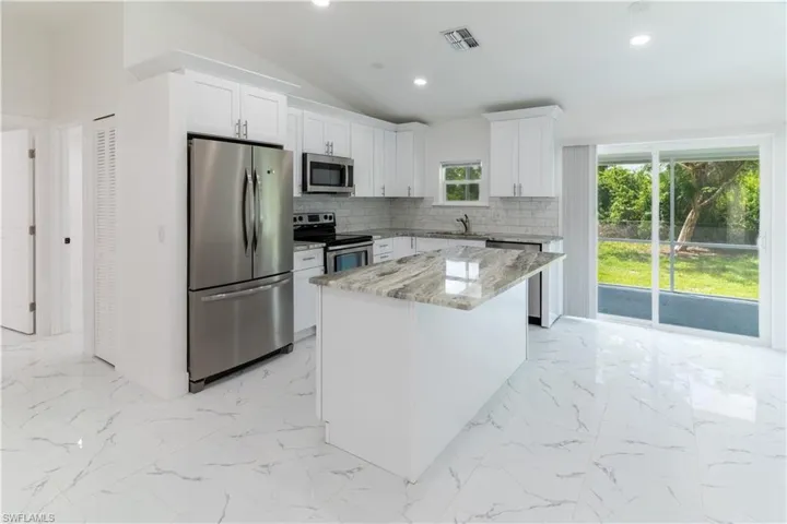 Kitchen with appliances with stainless steel finishes, tasteful backsplash, lofted ceiling, light stone countertops, and light marble finish floors