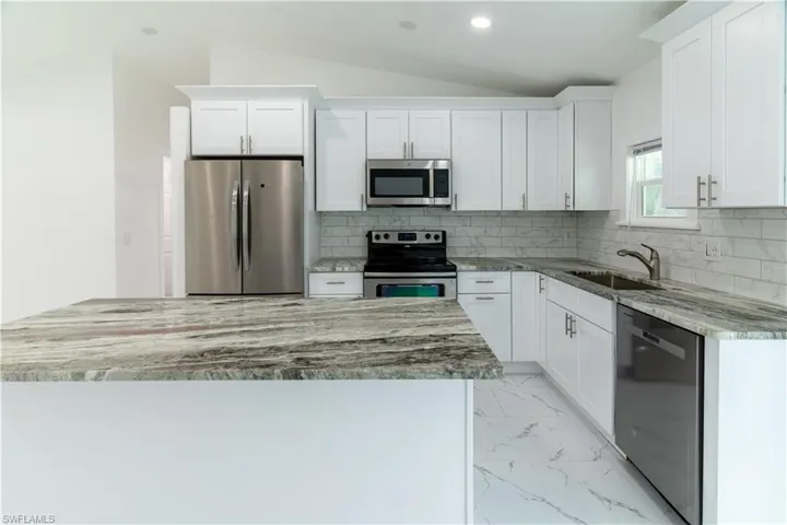Kitchen with appliances with stainless steel finishes, backsplash, light stone counters, light marble finish flooring, and white cabinetry