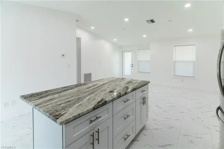 Kitchen featuring a center island, recessed lighting, light marble finish flooring, gray cabinets, and light stone counters