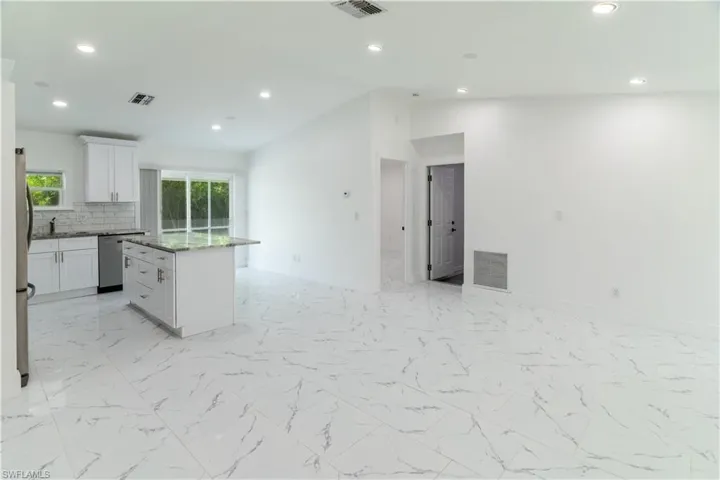 Kitchen with a kitchen island, white cabinetry, recessed lighting, light marble finish flooring, and light stone countertops
