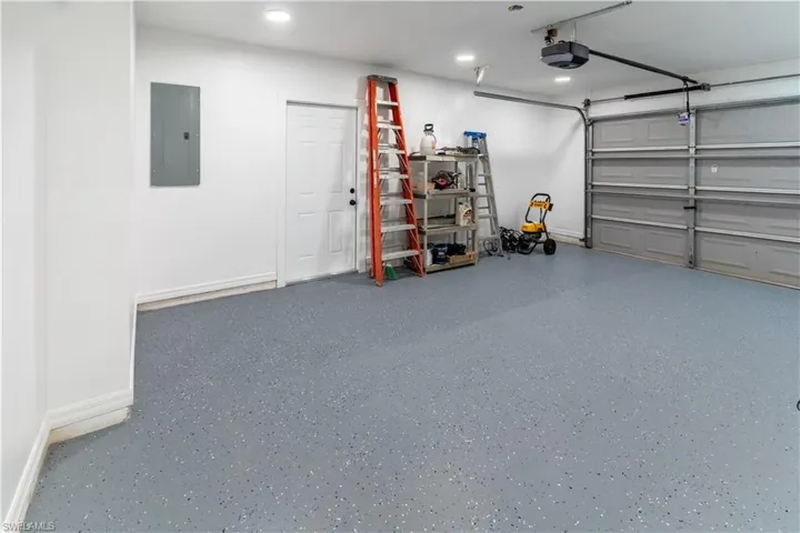 Garage with electric panel, recessed lighting, and a garage door opener