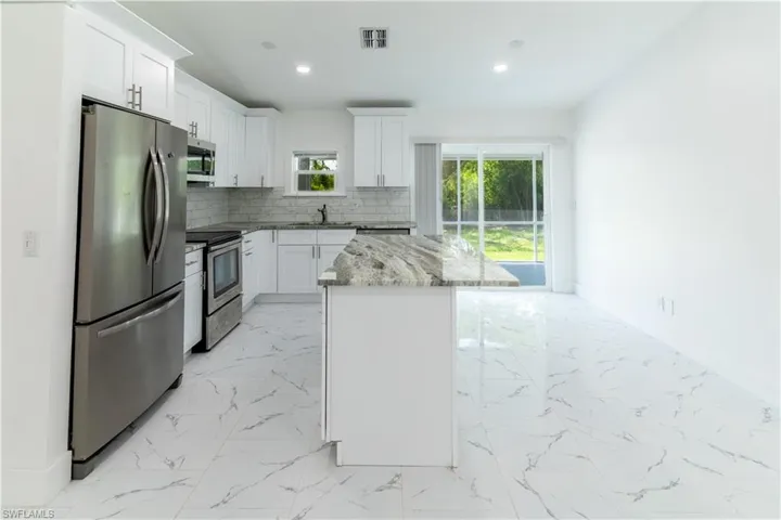 Kitchen with appliances with stainless steel finishes, light marble finish flooring, decorative backsplash, a kitchen island, and recessed lighting