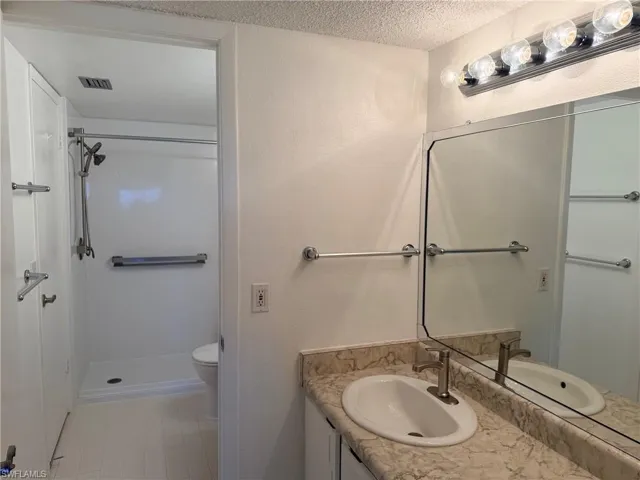 Bathroom vanity with a stone-patterned laminate countertop, undermount oval sink, chrome faucet, wall-width mirror, and a walk-in shower stall with an adjustable showerhead