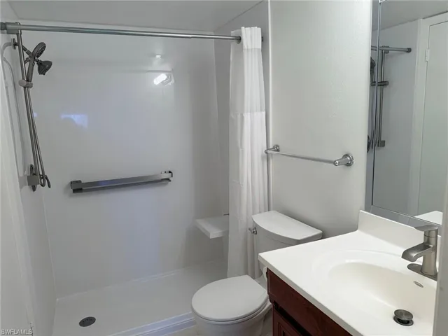 Bathroom featuring a walk-in shower with integrated bench seating, adjustable shower head, vanity with a solid-surface countertop, and brushed nickel hardware