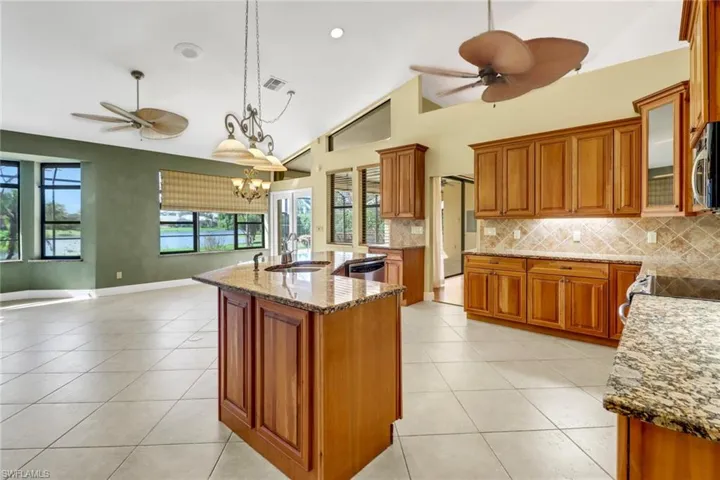 Kitchen with appliances with stainless steel finishes, high vaulted ceiling, hanging light fixtures, an island with sink, and ceiling fan