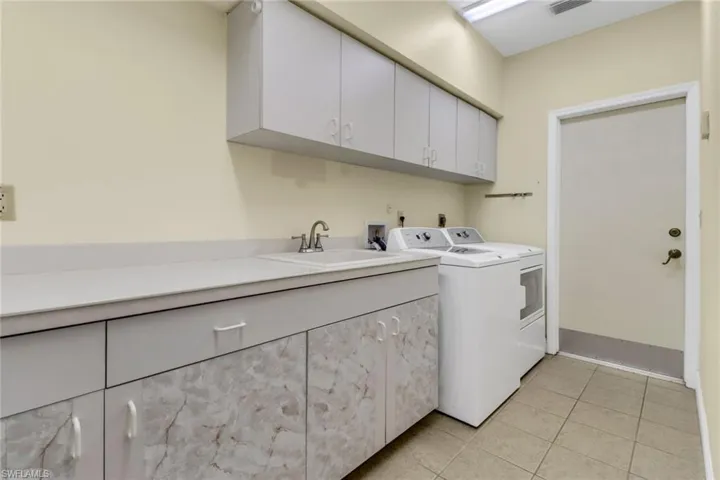 Laundry room featuring cabinets, light tile patterned floors, sink, and washing machine and clothes dryer