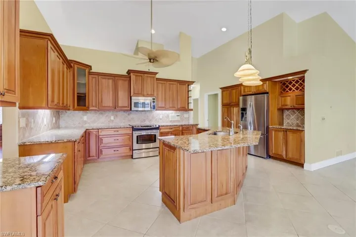 Kitchen featuring stainless steel appliances, backsplash, high vaulted ceiling, pendant lighting, and an island with sink