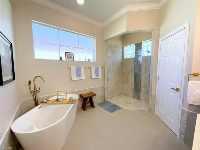 Bathroom featuring a soaking tub, crown molding, and a marble finish shower