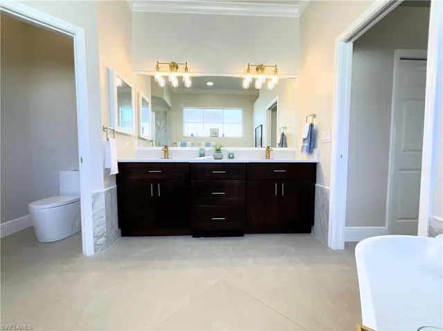 Full bathroom with double vanity, ornamental molding, toilet, and a freestanding bath