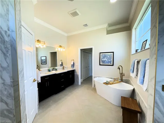 Full bathroom featuring crown molding, double vanity, visible vents, a freestanding tub, and tile patterned floors