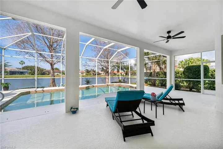 View of swimming pool featuring ceiling fan, a patio area, glass enclosure, and a water view