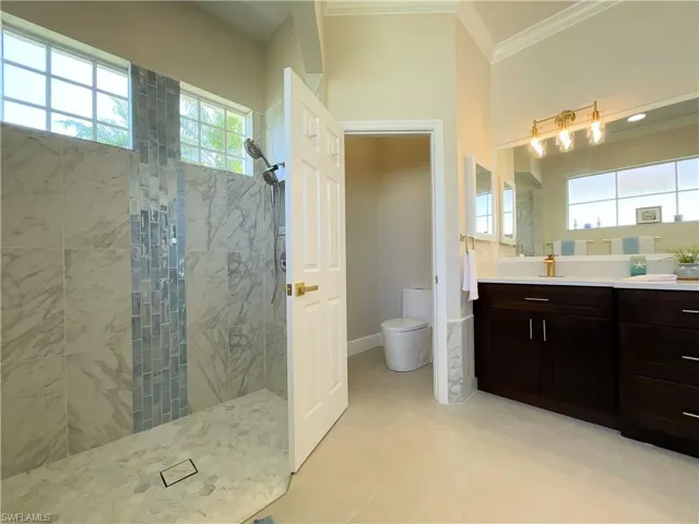 Full bath with toilet, vanity, baseboards, walk in shower, and crown molding