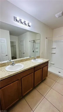 Full bathroom with tile patterned flooring, a shower, double vanity, and a closet