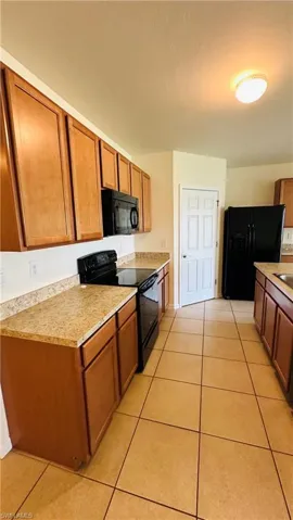 Kitchen with black appliances, light tile patterned floors, light countertops, and brown cabinets