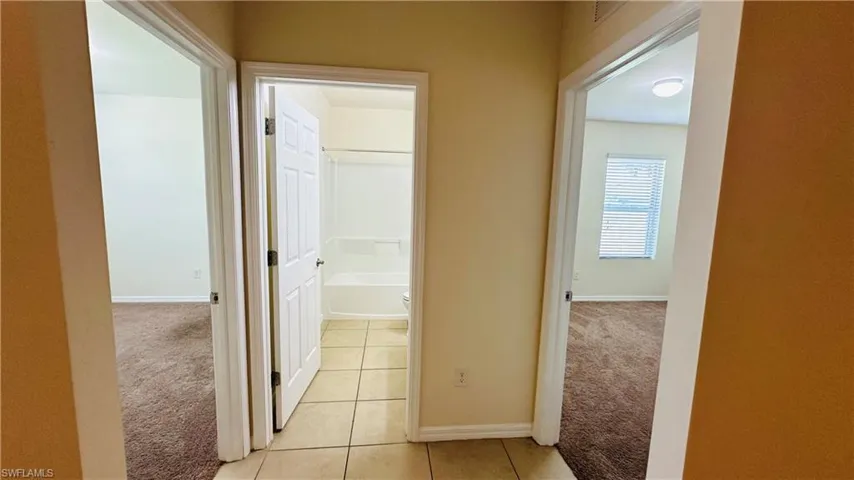 Hallway featuring light carpet and light tile patterned flooring