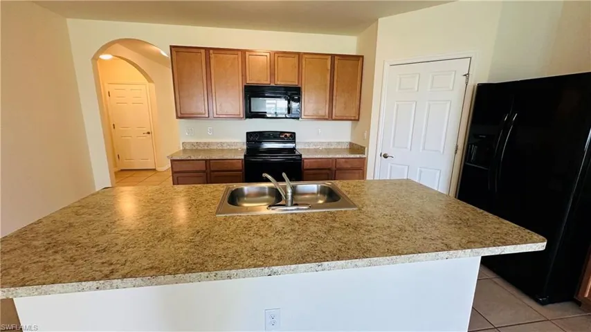 Kitchen with light tile patterned flooring, black appliances, and arched walkways