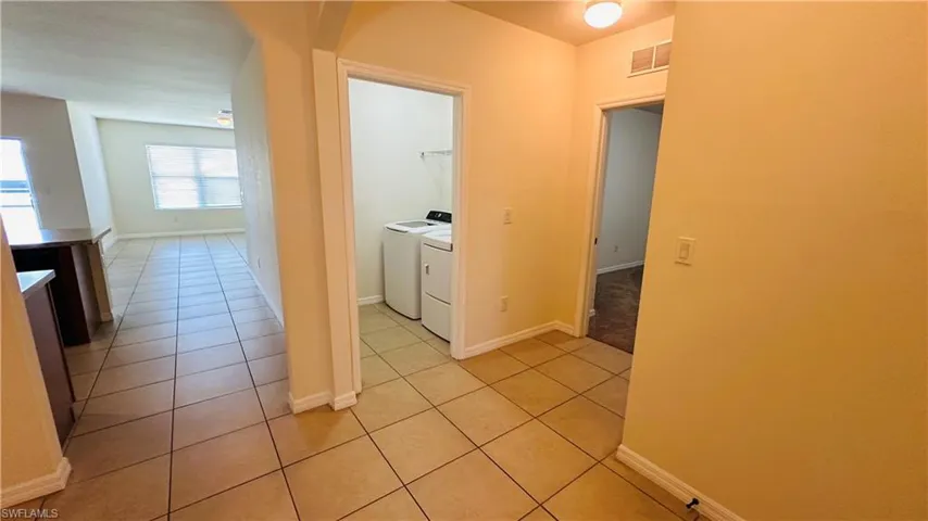 Hallway featuring independent washer and dryer, light tile patterned flooring, and arched walkways