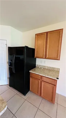 Kitchen featuring brown cabinets, light tile patterned floors, black fridge, and light stone countertops