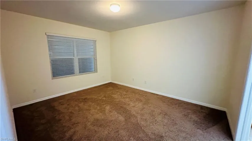 Unfurnished room featuring dark carpet and baseboards