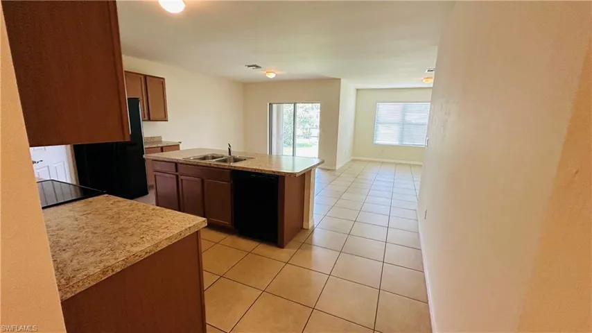 Kitchen featuring light tile patterned floors, black appliances, light countertops, and an island with sink