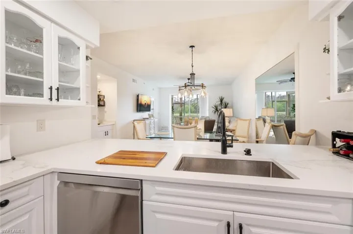 Kitchen with sink, dishwasher, white cabinetry, hanging light fixtures, and light stone counters