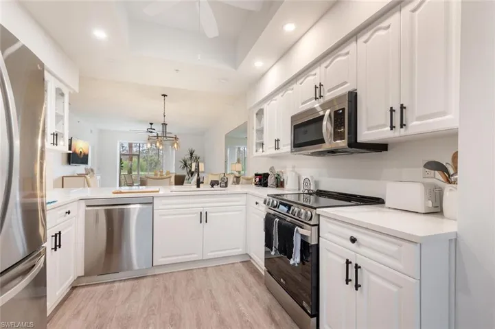 Kitchen featuring ceiling fan, hanging light fixtures, stainless steel appliances, white cabinets, and kitchen peninsula