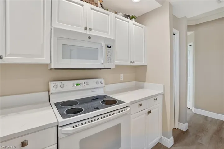 Kitchen featuring white appliances, white cabinetry, light wood-style flooring, and light stone countertops
