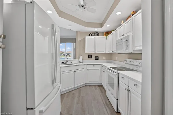 Kitchen featuring crown molding, white appliances, light countertops, a raised ceiling, and white cabinetry
