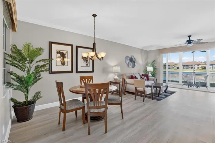 Dining space featuring light wood finished floors, ceiling fan, hanging lights, crown molding, and a water view
