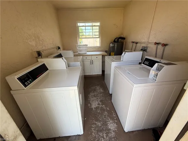 Dedicated laundry area featuring multiple top-loading machines, built-in cabinetry with a light-toned countertop, and a window providing natural light