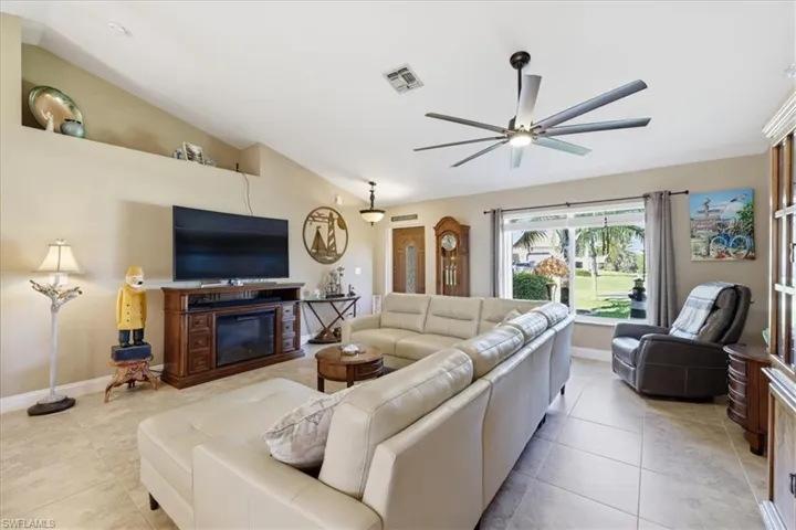 Living area featuring lofted ceiling, a ceiling fan, light tile patterned flooring, and a glass covered fireplace