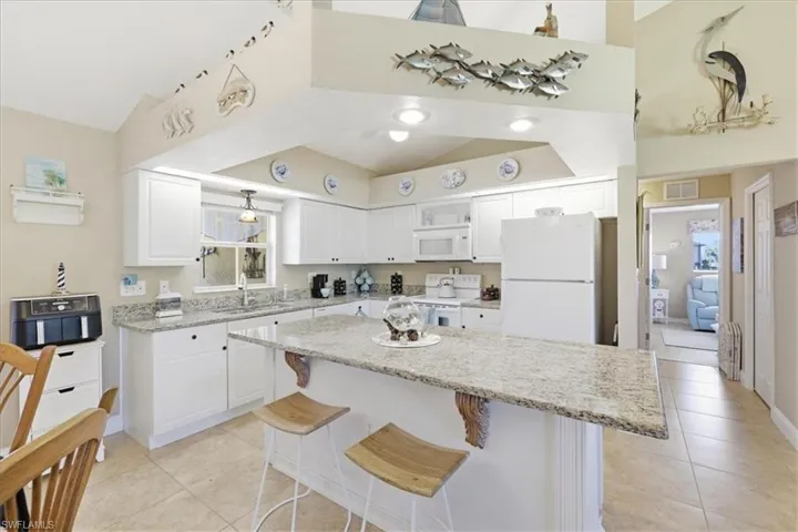 Kitchen featuring a breakfast bar, white cabinetry, light stone counters, white appliances, and a kitchen island